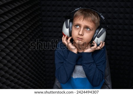portrait of smiling fair haired teenage boy in blue with headphones looking up hearing test. in a dark room, impurities against sound