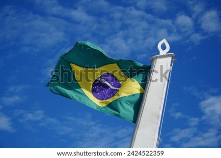 The Brazilian flag flies in the wind against a blue sky, isolated and bathed in sunlight. At the back of a cargo ship traveling up and down the Amazon River in Brazil. Juriti, Para, Brazil. Royalty-Free Stock Photo #2424522359