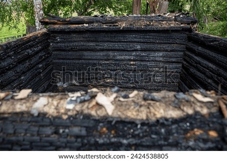 Charred wooden logs of a barn, bathhouse, house after a fire.