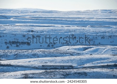 A Northern train passing through the Yorkshire Dales National Park near Horton in Ribblesdale on a beautiful winter day with bright sun and lots of snow on the ground and over the fields. Royalty-Free Stock Photo #2424540305