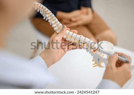 Picture of a close-up of an orthopedic doctor pointing at a spinal model and explaining to a female patient her spinal problems. Health care concept and aging and back pain