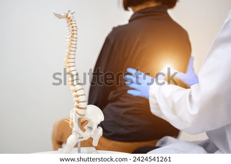An orthopedic surgeon or therapist is showing a spinal model and explaining to a female patient her spinal problems. Back pain and health care concept