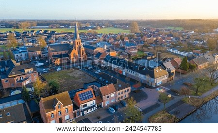 This aerial shot captures the quaint town of Rijkevorsel during the soft light of dusk. The Sint Jozef Church, with its towering spire, stands prominently among the surrounding residential buildings
