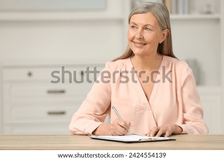 Smiling senior woman signing Last Will and Testament at wooden table indoors. Space for text