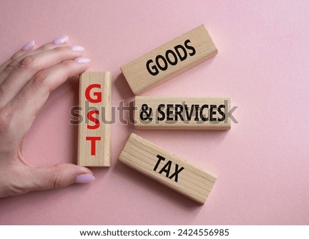 GST - Goods and Services Tax symbol. Concept word GST on wooden blocks. Businessman hand. Beautiful pink background. Business and GST concept. Copy space.