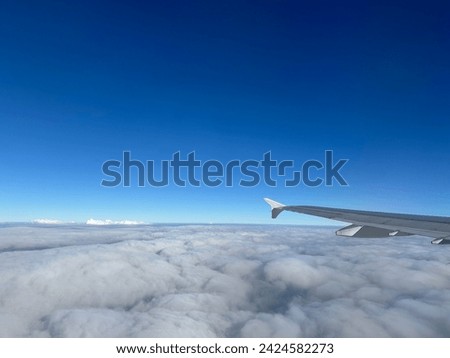 An airplane wing with winglet in the blue sky above the clouds, captured from the airplane window Royalty-Free Stock Photo #2424582273