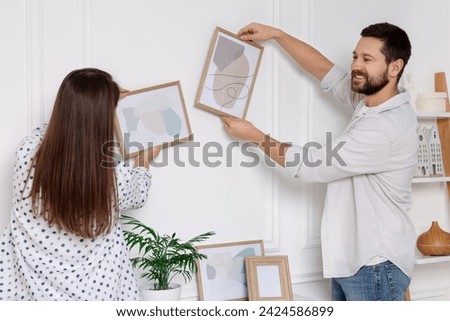 Man and woman hanging picture frames on white wall at home