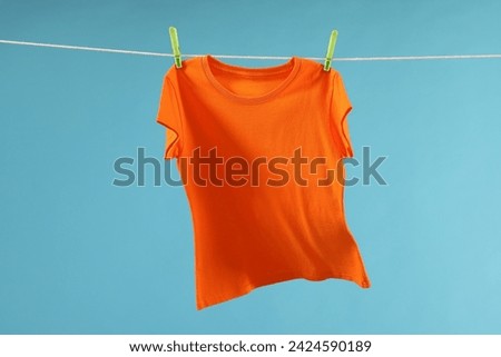 One orange t-shirt drying on washing line against light blue background Royalty-Free Stock Photo #2424590189