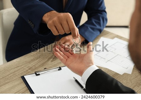 Real estate agent giving key to client at table in office, closeup