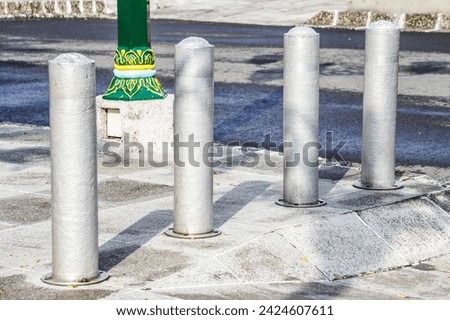 Metallic long inground bollard pole barrier between asphalt road and sidewalk to protect pedestrians and roadside decoration. Town square, urban, city, infrastructure. In Ground Metal Bolard. Royalty-Free Stock Photo #2424607611