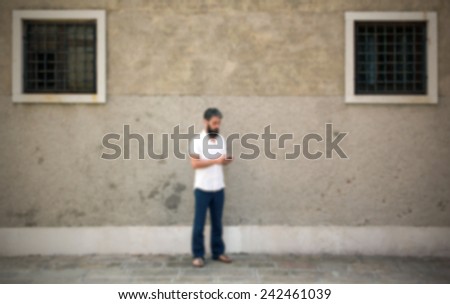 Man with his phone, empty wall on the background. Intentionally blurred post production.