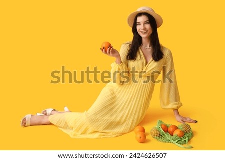 Beautiful young woman in stylish yellow dress and string bag with oranges on color background Royalty-Free Stock Photo #2424626507