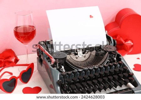 Beautiful composition with vintage typewriter, glass of wine and decor for Valentine's day on table near pink wall