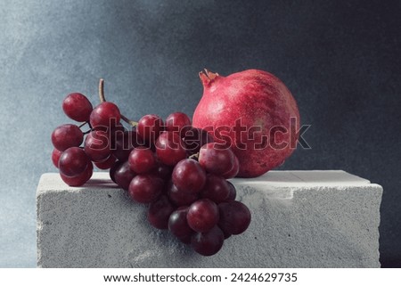 Red Grape Bunch and Whole Pomegranate on Textured Concrete Slab Royalty-Free Stock Photo #2424629735