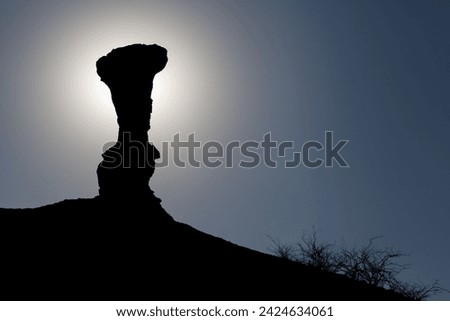 Backlit silhouette of a geological formation against the background of a blue sky. This geological formation blocks the sun and creates a halo of glare that produces a black silhouette. Royalty-Free Stock Photo #2424634061