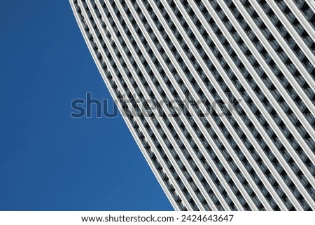 Minimalistic photo of a part of a modern building with repetitive pattern on its exterior stands out against the clear blue sky.