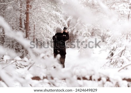 Middle aged hiker in winter forest taking a photo with his mobile phone. Man taking selfie in snowy forest with blurred out background