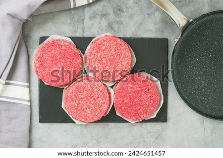 Burger patties in plastic conteiner, and frying pan close-up. Fresh raw burger patties close-up on a grey stone background, flat lay with copy space Royalty-Free Stock Photo #2424651457