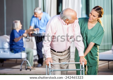 Happy female caretaker assisting senior man in using Zimmer frame at nursing home yard Royalty-Free Stock Photo #242465323