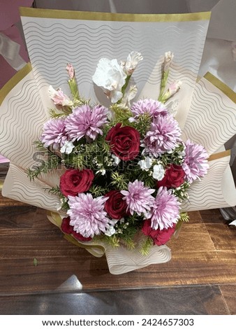 The image is a bouquet of flowers displayed in a vase on a wooden table. The arrangement includes various types of flowers and is likely used as a decorative centerpiece.