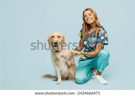 Full body young veterinarian woman wear uniform stethoscope heal exam hug cuddle embrace retriever dog hold paw isolated on plain pastel light blue background studio portrait. Pet health care concept