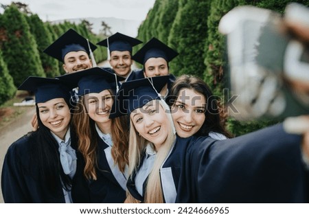 Proud graduates in park wearing caps and gowns, create memories while celebrating their bachelor’s degrees. Faculty faculty colleagues and friends take a group selfie. Royalty-Free Stock Photo #2424666965