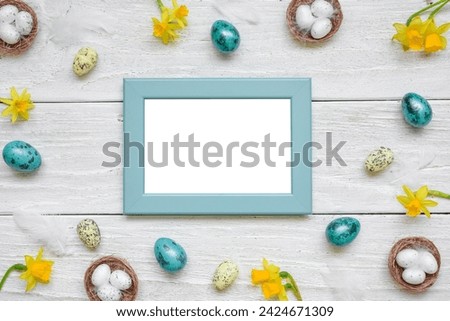 Easter picture photo frame with spring yellow Narcissus flowers and easter colorful eggs on white wooden background. Mock up. Flat lay. Top view with copy space