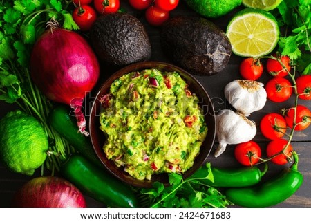 Bowl of Guacamole Surrounded by Fresh Ingredients: Guacamole with Hass avocados, jalapeno peppers, cherry tomatoes, and other ingredients
