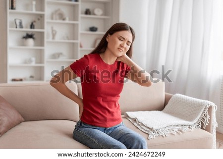 Young Asian Woman Suffering Neck And Back Pain At Home, Sick Korean Female Rubbing Painful Sore Zones And Frowning, Massaging Aching Areas While Sitting On Couch In Living Room, Copy Space