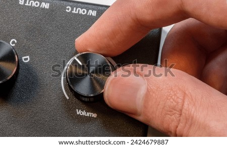Anonymous man fingers finely tuning a volume knob on a sleek audio device control panel, adjustment of sound levels, gain control, turning music up, or turning down, sound controls abstract concept Royalty-Free Stock Photo #2424679887