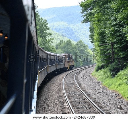 View from caboose looking forward of an old train going around the corner surrounding by green trees and forests Royalty-Free Stock Photo #2424687339