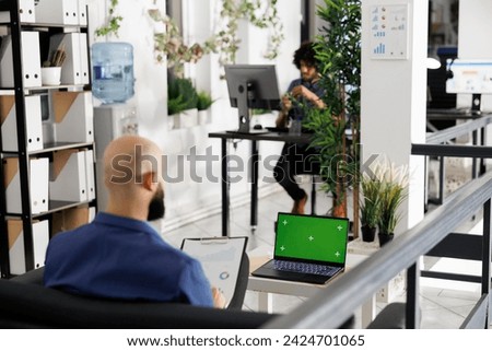Executive analyzing reports, developing strategy and using laptop with green screen. Entrepreneur working at corporate portable computer with chroma key display in coworking space