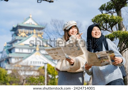 Travel, muslim travel, woman girl tourist Two Asian friends but different religions walking and visitor learning about history at Osaka Castle, landmarks in Japan and Osaka, holiday lifestyle.