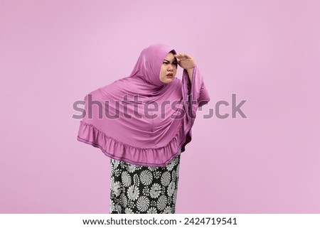Photo of  asian woman holding hand above her eyes and looking into copy space looking into distance expecting and searching for something with arm akimbo and smile face use for advertising
