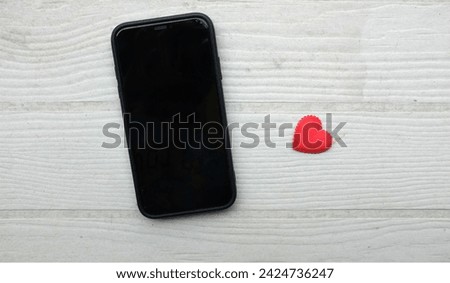 A black smartphone,phone ,mobile with a heart icon, surrounded by small red hearts isolate on a wooden table white backdrop .minimalist trend.valentines day,dating mobile application, digital online