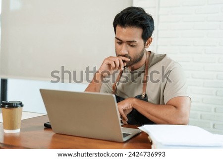 Multiethnic business men in beige shirts sitting working in of laptop, looking thoughtful, hand touching his mouth, had phone documents. croissant brown disposable coffee cup. small business cafe
