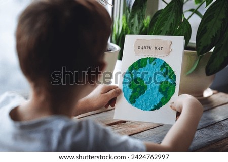 Children's craft for the Earth Day celebration. Little boy holding handmade simple postcard with a picture of our Planet made of plasticine. Concept of environment education for kids in kindergarten