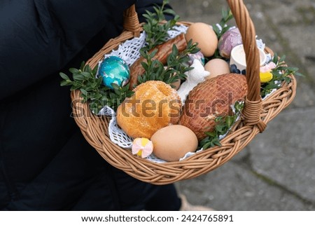 Woman holding Easter basket for blessing in a church. Traditional woven wicker Paschal basket filled with various food, ready to be blessed by a priest as part of the Easter tradition. Royalty-Free Stock Photo #2424765891
