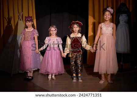 Full length portrait of group of children actors standing on stage holding hands for final bow at school play in theater Royalty-Free Stock Photo #2424771351