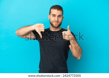 Young handsome caucasian man isolated on blue background making good-bad sign. Undecided between yes or not