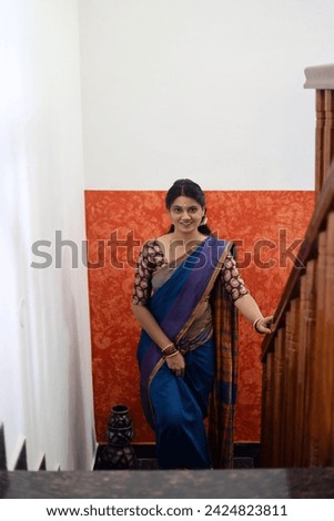 A selective focus of the face of a south Indian young woman or girl in a blue colored saree posing on stairs or steps inside a house.