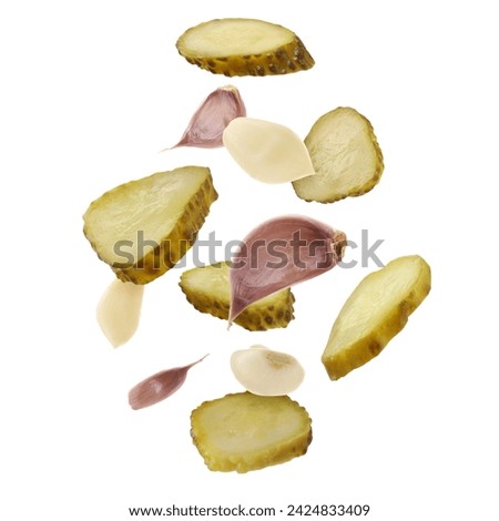 Slices of tasty pickled cucumbers and garlic falling on white background