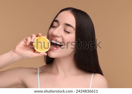 Beautiful young woman with piece of orange on beige background