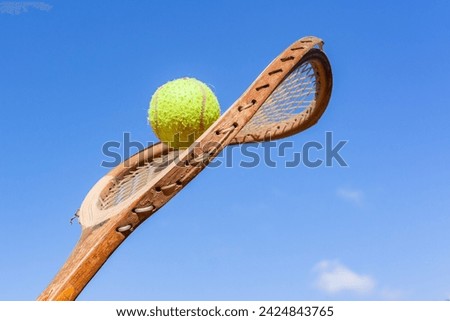 Old Tennis Racket Bent Twisted Frame with Ball attached closeup blue sky history abstract concept of sport. Royalty-Free Stock Photo #2424843765