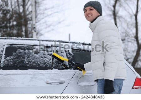 Man cleaning snow from car with brush outdoors, low angle view