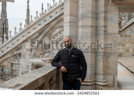 Travel, holidays and winter vacations concept - Urban bliss: A happy young man poses with delight on the roof of Milan Cathedral, capturing the city's allure with a radiant smile