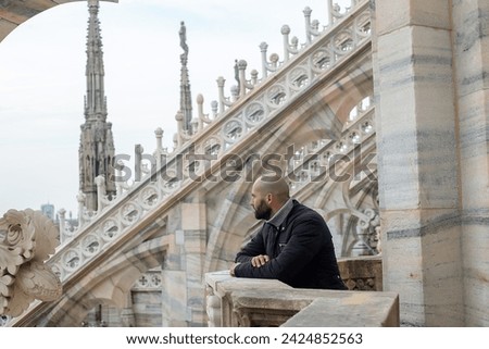Travel, holidays and winter vacations concept - Cityscape serenity: A beaming tourist man finds peace on the roof of Milan Cathedral, his smile adding warmth to the urban skyline