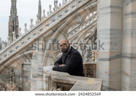 Travel, holidays and winter vacations concept - Sky-high happiness: A cheerful tourist man enjoys the rooftop view of Milan Cathedral, his smile reflecting the city's magic and allure