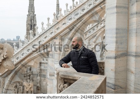 Travel, holidays and winter vacations concept - Chic panorama: A stylish young man in Milan smiles joyfully on the roof of Milan Cathedral, epitomizing the city's charm and elegance