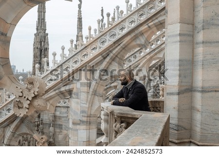 Travel, holidays and winter vacations concept - Milan adventure: A carefree young man embraces Milan's beauty from above, his smile reflecting the joy of exploration on the roof of Milan Cathedral